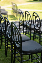 Elegant black chairs are neatly arranged for an outdoor wedding ceremony, surrounded by lush greenery and a serene atmosphere