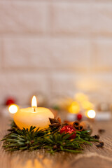 Burning white candle on Christmas tree branches and lights on a wooden table.