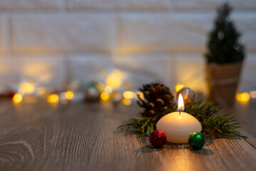 Burning white candle on Christmas tree branches and lights on a wooden table.