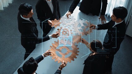 A diverse business team collaborates on innovative ideas using gears and a digital security overlay, showcasing teamwork and modern technology in a professional office. Raster