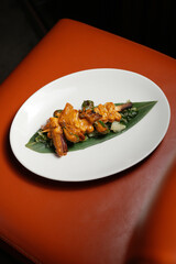 An overhead, vertical shot of a single grilled skewer, chicken or seafood coated in a creamy orange sauce