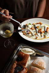 Young woman having dinner with appetizer of anchovies, cream sauce, and croutons on a white plate,...