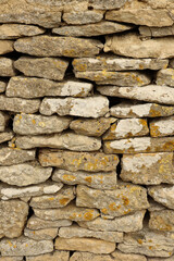 Dry stone walling detail showing rough textured rock surface with various earthy tones and yellow lichen spots