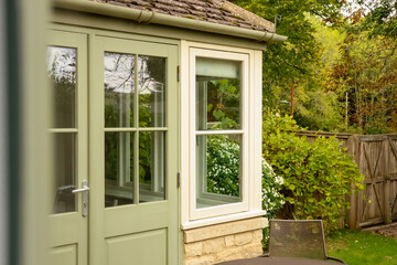 Garden room exterior with pale green door and window reflecting surrounding nature. Cotswolds...