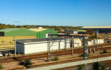 Obraz premium Railway tracks passing industrial warehouses under a sunny blue sky, urban transportation infrastructure