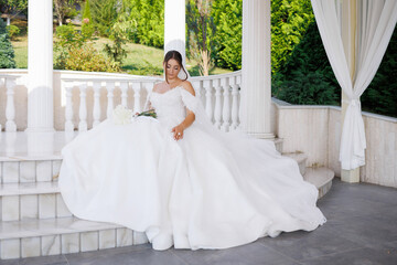 Bride in elegant wedding dress sitting gracefully on marble steps at outdoor venue
