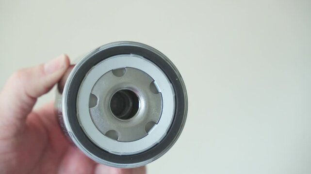 A close-up of an automotive oil filter being held in a hand, focused on the thread, gasket, and internal structure.