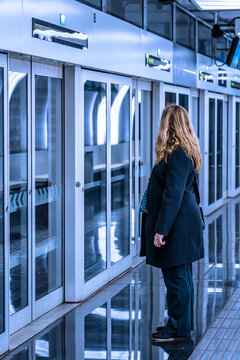 Rear view of a woman waiting for a train next to the automatic doors of a platform at a futuristic metro station illuminated with blue lights at the Ciutat de la Just&iacute;cia station in Hospitalet, Barcel