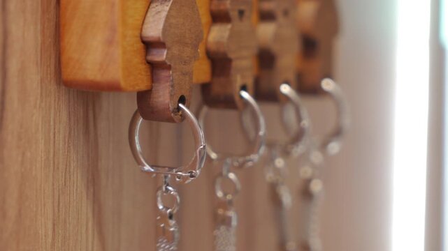 Multiple silver keychains hang from decorative wooden hooks on a wooden wall. This image captures an organized and ready state of daily essentials in a home setting.