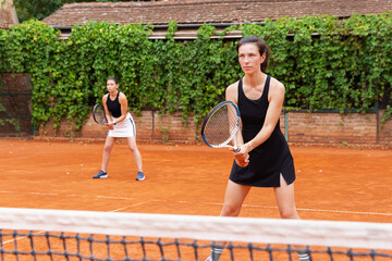 Two tennis players ready for a doubles match on clay court. Concept of teamwork, focus and competitive spirit in outdoor sports environment.