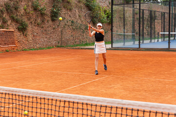 Obraz premium Woman hitting tennis ball on clay court. The photo conveys concentration, movement, and the dynamic balance between power and control in sport.