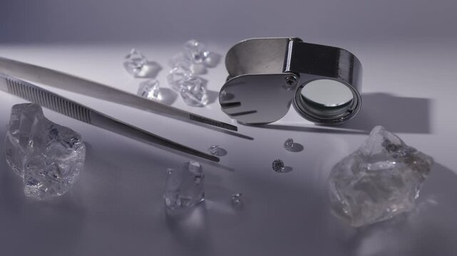 Magnifying glass and tweezers with diamonds on white surface in blue light.