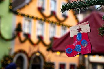 Obraz premium Close-up of a handmade children’s Christmas ornament painted by a child, hanging on a tree branch. Blurred festive background with a decorated house, perfect space for text or holiday greeting design.
