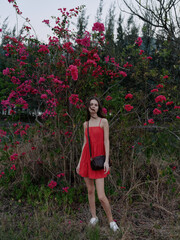young woman in red dress standing near blooming pink flowers, natural outdoor setting with greenery...