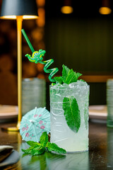 Mojito with mint and lime on dark table. Classic mojito with mint leaves, lime, and ice served in tiki glass on restaurant table.