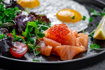 Scrambled eggs with salmon and salad greens close up. Close-up of breakfast plate with scrambled eggs, salmon slices, red caviar, and fresh greens.