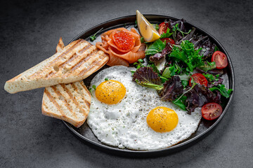 Fried eggs with salmon, caviar, and salad top view. Top view of breakfast with fried eggs, salmon, red caviar, green salad, and toast bread.