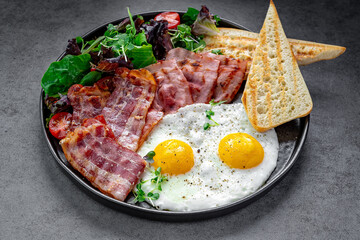 Fried eggs and bacon breakfast close up. Close-up of classic breakfast with fried eggs, crispy bacon, toasted bread, and salad greens on a plate.