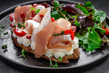 Bruschetta with prosciutto and cream cheese close up. Close-up of toasted bread with cream cheese, prosciutto, and cherry tomatoes served with salad greens.
