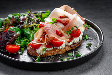 Bruschetta with prosciutto, cheese, and tomatoes. Italian bruschetta with cream cheese, prosciutto, sun-dried and fresh cherry tomatoes served with green salad.