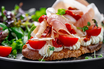Bruschetta with prosciutto and tomatoes side view. Side view of Italian bruschetta topped with prosciutto, sun-dried tomatoes, and cream cheese on toasted bread.