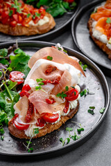 Bruschetta assortment with prosciutto and salmon. Assorted bruschettas with prosciutto, salmon, and tomato topping served with green salad on black plates.