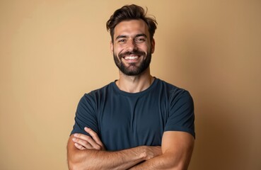 Obraz premium Bearded man in dark blue t-shirt stands with arms crossed smiling. He looks confident and happy, ready for new challenges. A strong, friendly individual.