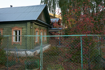 A rural wooden house with window frames. Beyond the fence, in the front garden, a rowan tree with...