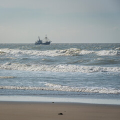 single ship is sailing on the North Sea, ship, sails and waves shine in the evening light, North Sea beach before sunset with waves of the ocean
