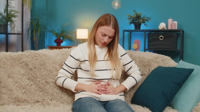 Caucasian woman girl at home sofa experiencing severe stomach monthly menstrual pain cramps feeling stressed. Trying relief from discomfort indigestion overeating anxious worried searching calm remedy