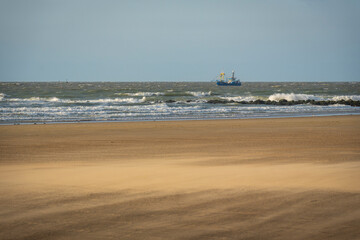 single ship is sailing on the North Sea, ship, sails and waves shine in the evening light, North Sea beach before sunset with waves of the ocean