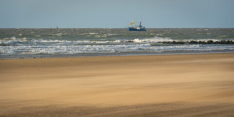 single ship is sailing on the North Sea, ship, sails and waves shine in the evening light, North Sea beach before sunset with waves of the ocean
