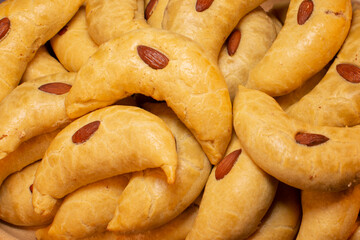 A pile of golden crescentshaped pastries, each topped with a flavorful almond, is elegantly displayed