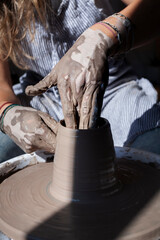 Muddy hands shaping interior of tall clay vessel on wheel