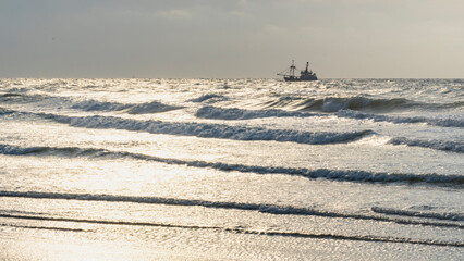 single ship is sailing on the North Sea, ship, sails and waves shine in the evening light, North Sea beach before sunset with waves of the ocean