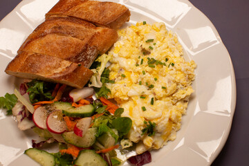 On a plate, you can find a delightful combination of scrambled eggs, crispy toast, and a vibrant fresh salad