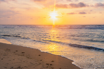 Sunset over stormy North Sea beach with reed grass bushes, orange-red sky over the dark blue ocean, panorama with sandy beach and blowing grass in the wind, storm at sunset over wavy water