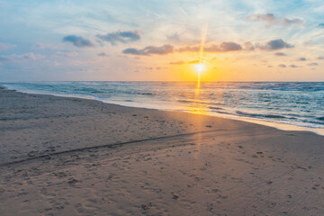 Sunset over stormy North Sea beach with reed grass bushes, orange-red sky over the dark blue ocean, panorama with sandy beach and blowing grass in the wind, storm at sunset over wavy water