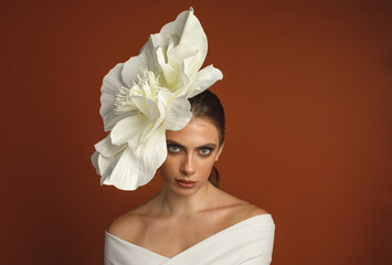 Elegant woman wearing a giant white paper flower headpiece against warm brown background. Minimal...