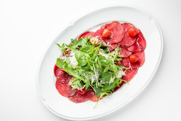 Beef carpaccio with arugula, cherry tomatoes, Parmesan cheese, and olive oil on a white plate. Classic Italian appetizer, fresh and elegant presentation.