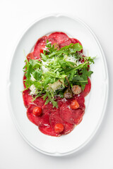 Beef carpaccio with arugula, cherry tomatoes, Parmesan cheese, and olive oil on a white plate. Classic Italian appetizer, fresh and elegant presentation.