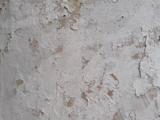 Old wall with cracked and peeling white paint. Weathered plaster texture showing natural decay and rough surface, perfect for grunge backgrounds, vintage or architectural design projects.