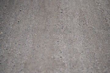 Close-up image of a textured dirt road with a rough, grayish-brown surface, featuring small pebbles and a natural, weathered look, ideal for rural or outdoor settings.