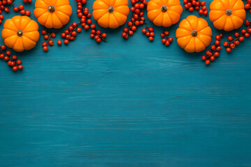 Autumn pumpkins and red berries on vibrant turquoise wooden background creating festive fall harvest decoration border