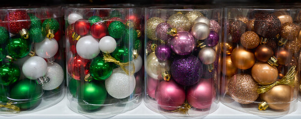 Colorful Christmas ornaments in transparent plastic boxes. Shiny and glittery baubles in red, green, gold, pink, and bronze tones, ready for decorating a festive Christmas tree.