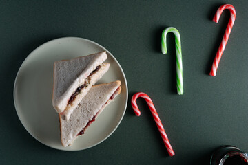 A holiday sandwich of white bread, cranberry sauce, and savory stuffing, served on a round plate against a dark green background with candy canes