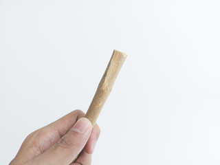Hand holding a natural miswak stick isolated on white background, traditional herbal toothbrush for oral hygiene and eco-friendly dental care.
