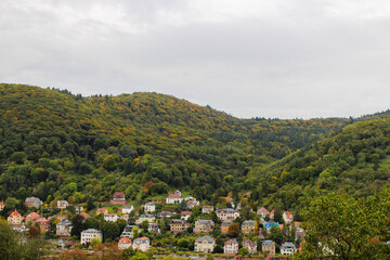 shot from distance from the top of a mountain showing a small german village laying within green mountains on a misty autumn day 