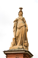 female beige statue with cape and helmet on a red stone base on a white background
