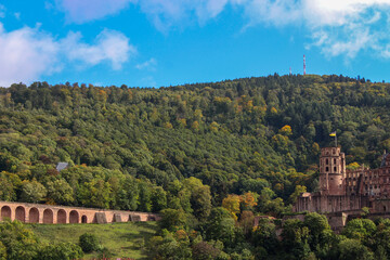shot from distance showing the heidelberg castle to the right surrounded by green autumn trees on a slightly cloudy sunny day 